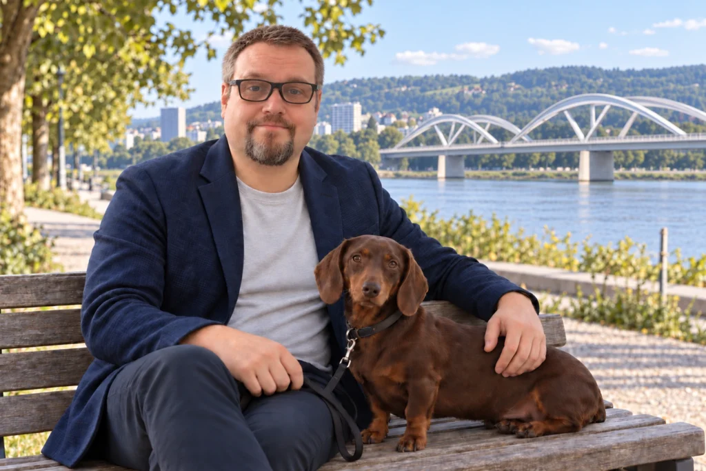 Herbert Röblreiter und Kurzhaardackel Kira auf einer Bank, im Hintergrund Urfahr und die neue Eisenbahnbrücke